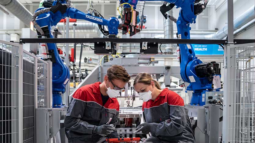 Zwei Personen arbeiten mit Roboterarmen an einem Werkstück.