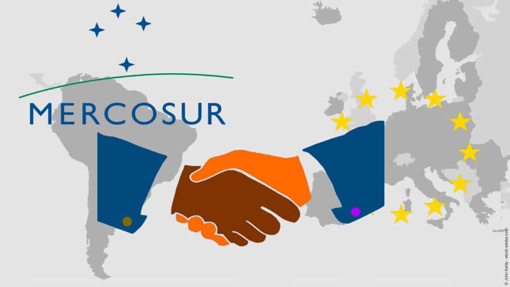 Handelsabkommen zwischen Mercosur und der EU - Auf den Landkarten von Südamerika und Europa befinden sich die jeweiligen Symbole. Davor die Illustration eines Händedrucks als Symbol für einen Vertrag.