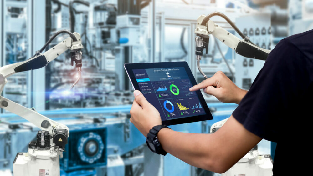 Intelligentes Industrie-Steuerungskonzept. Hände halten ein Tablet auf einer unscharfen Automatisierungsmaschine als Hintergrund.