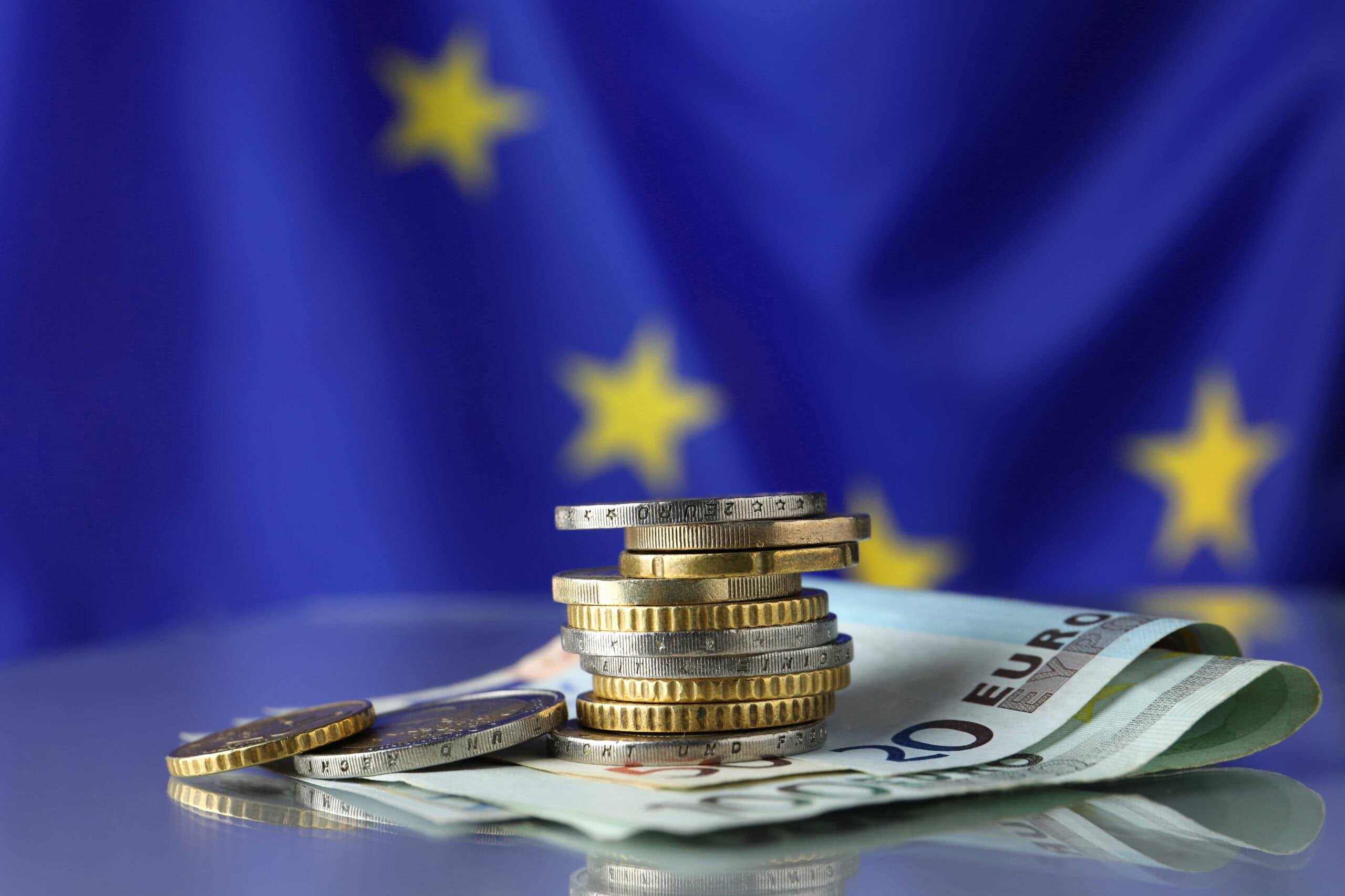 Coins and banknotes on table against European Union flag, space for text
